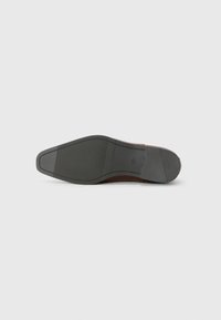 Suela de zapato de cuero marrón con una superficie de goma negra texturizada. Presenta una forma suave y afilada, con detalles de costura a lo largo de los bordes.