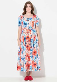 Robe florale avec un devant à boutons, des manches courtes bouffantes et une jupe fluide dans des couleurs vives rouge, bleu et blanc avec un motif de grandes fleurs.