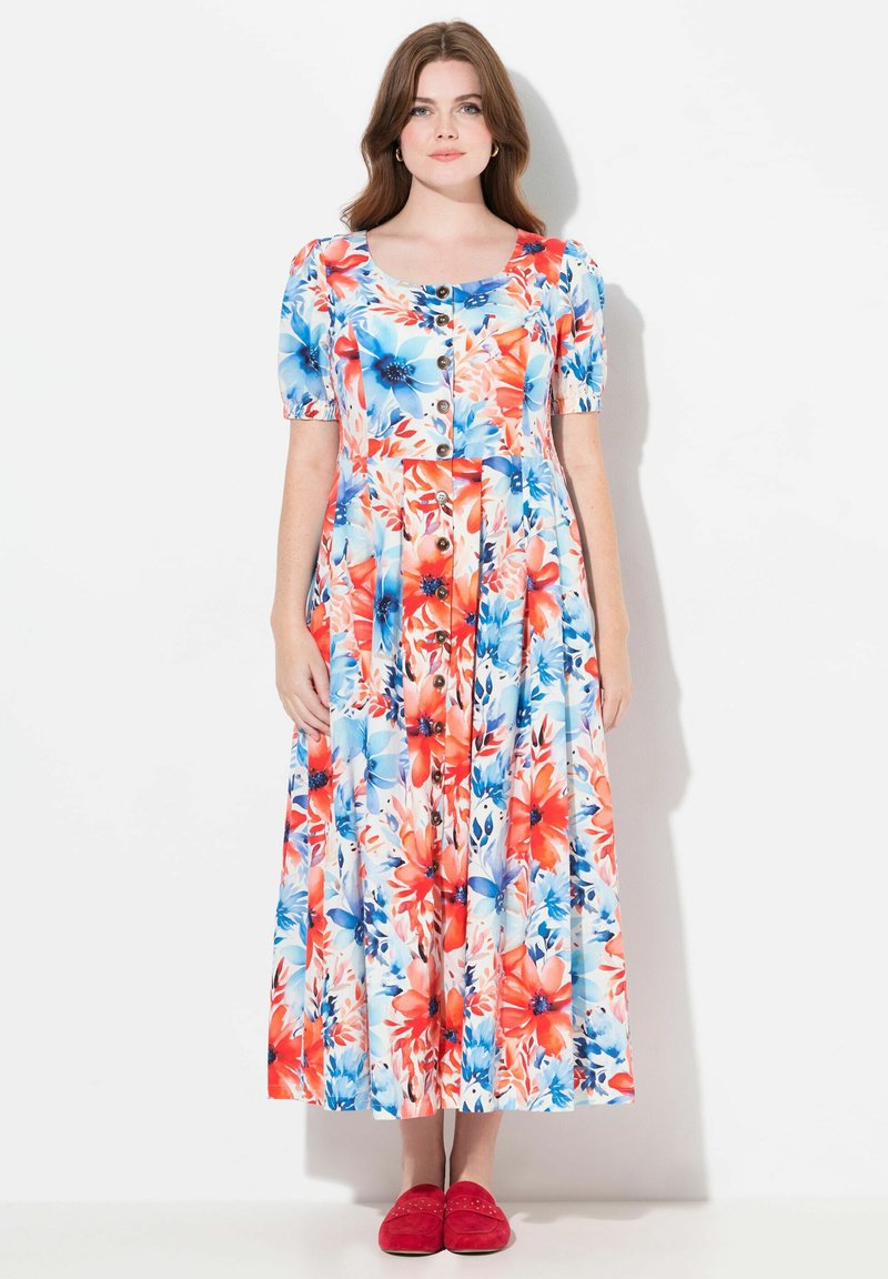 Robe florale avec un devant à boutons, des manches courtes bouffantes et une jupe fluide dans des couleurs vives rouge, bleu et blanc avec un motif de grandes fleurs.