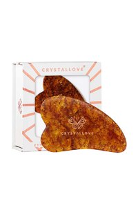 Amberowy gua sha o gładkim, zaokrąglonym kształcie i sylwetce przypominającej motyla, zapakowany w ozdobne białe pudełko.