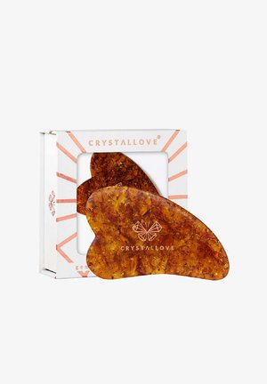 Amberkleurige gua sha-tool met een glad, rond ontwerp en een vlinderachtig silhouet, verpakt in een decoratieve witte doos.