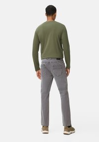 Jeans en denim gris avec une jambe droite et des poches arrière, associés à une chemise à manches longues olive et des baskets marron.