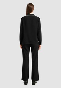 Maglione nero a maglia con colletto e dettagli in perle, abbinato a pantaloni neri svasati. Texture liscia, design aderente. Nessun motivo visibile.