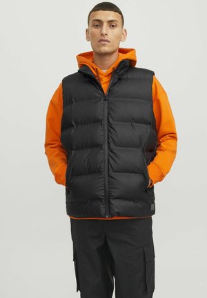 Sort puffer-vest med polstrede sektioner, lynlås foran og sidelommer, båret over en orange hættetrøje, parret med sorte cargo-bukser.