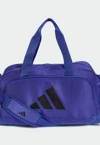 Μπλε αθλητική τσάντα Adidas με μαύρο λογότυπο, διπλές λαβές, ρυθμιζόμενο ιμάντα ώμου και μπροστινή τσέπη με φερμουάρ.