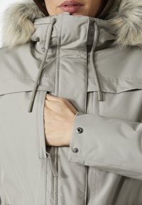 Light grey padded jacket with a faux fur hood, adjustable drawstrings, and snap closure on cuffs. Textured fabric and zippered pocket detail.