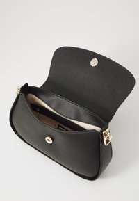 Sac à main structuré noir avec une surface texturée, quincaillerie dorée, fermeture magnétique et une poche intérieure. Le design ouvert révèle un intérieur beige.
