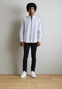 Lichtblauw verticaal gestreepte overhemdbloes, zwarte slim-fit broek en witte sneakers. Platte kraag en een relaxte pasvorm. Soepele stoftextuur.