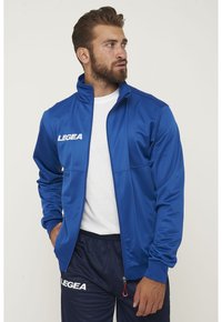 Giacca sportiva blu realizzata in tessuto liscio, caratterizzata da un colletto alto, chiusura con zip e logo LEGEA bianco sul petto.