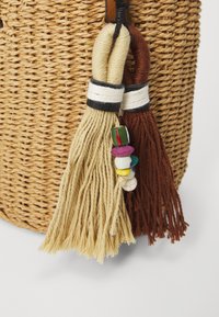 Borsa rotonda intrecciata in paglia con nappe marroni e beige e piccole perline colorate. Presenta dettagli in bianco e nero sulle nappe.