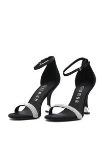 Sandalias de tacón negro con material de ante, punta abierta y una tira de strass brillante. Correa en el tobillo ajustable y tacón de aguja delgado.