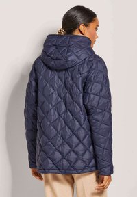 Navyblaue gesteppte Pufferjacke mit Kapuze, Rautenmuster und Reißverschluss, entworfen für Wärme und Komfort.