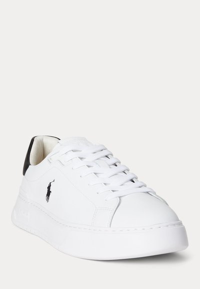 Valge madala säärega tennisejalanõu valgete paelte, musta kannataberi ja musta polo mängija logoga küljel, näidatud kerge kaldega.