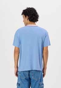 Camiseta de manga corta azul claro con cuello redondo y ribete rojo en el cuello. Tejido suave con un corte relajado.