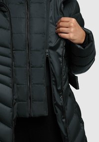Polstret jakke i mørkegrå med et quiltet design og dobbelt lynlås. Stoffet virker glat med en subtil glans.