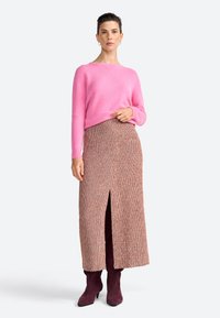 Maglione rosa a maglia con vestibilità comoda, abbinato a una gonna maxi marrone con motivo e spacco frontale. Il modello indossa stivaletti borgogna.
