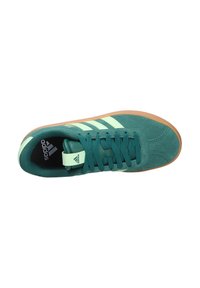 Zapatillas de ante verde con tres rayas verde claro, cordones texturizados y suela de goma. Logo en la lengüeta y cuello acolchado.