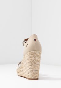 Beige hoge hak schoenen met een gevlochten jutenzool en een gladde stoffen bovenkant. Eigenschappen zijn een zilveren gesp en een klein logopatch op de hak.