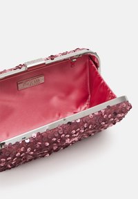 Rosa paljetterad kuvertväska med en glänsande metallram och lås. Inredningen har en slät rosa satinfoder. Öppen vy visar det inre utrymmet.