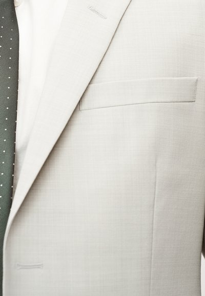 Ανοιχτό γκρι σακάκι με λείο υφή, μία τσέπη στο στήθος και καθαρές άκρες, συνδυασμένο με πράσινη γραβάτα με λευκές πουά βούλες.