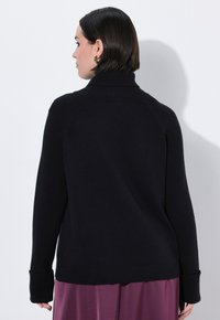 Maglione nero a coste con colletto alto, caratterizzato da maniche lunghe e una vestibilità rilassata. Texture morbida, design minimalista e lunghezza cropped.