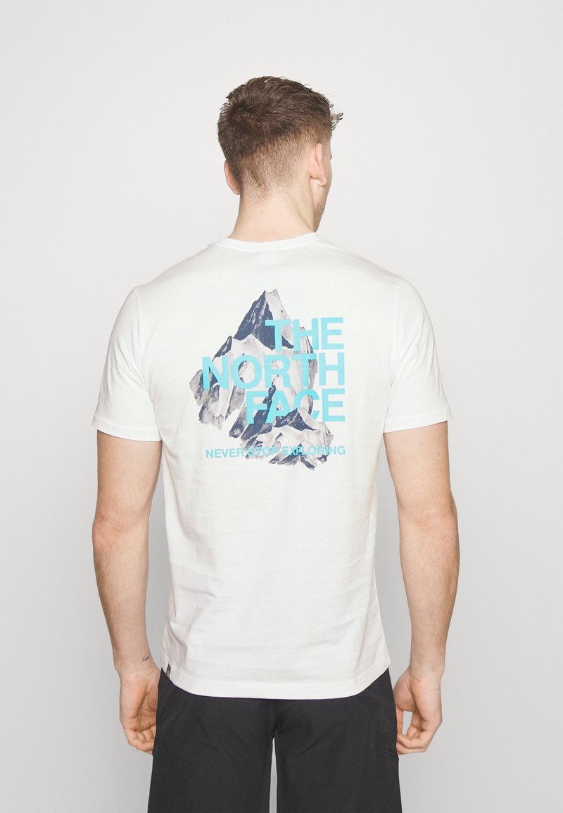 White cotton t-shirt featuring a mountain graphic in blue and dark gray on the back, with "THE NORTH FACE" and "NEVER STOP EXPLORING" text.