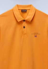Oranges Poloshirt aus strukturiertem Stoff, mit einem Zwei-Knopf-Verschluss, schwarzen Knöpfen und einem gestickten Logo mit einem Akzent in Form der norwegischen Flagge.