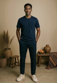 Navyblauwe katoenen t-shirt met een zak, gecombineerd met bijpassende tapse broek. Het model draagt lichte sneakers. De achtergrond heeft decoratie.