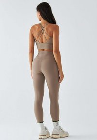 Brązowy sportowy krótki top z krzyżującymi się ramiączkami, zestawiony z wysokim stanem legginsów. Całość uzupełniają trampki i skarpetki z zielonym obszyciem.