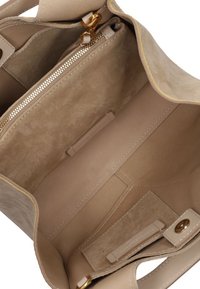 Interieur van een beige suède handtas met een gladde voering, een gouden rits en een insteekvak. Minimalistisch ontwerp met subtiele stikdetails.