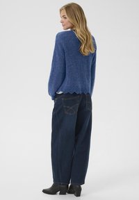 Blue knit sweater with a scalloped hem, paired with loose-fitting dark jeans featuring rear pockets, and black heeled ankle boots.