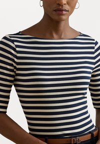 Tumesinine ja kreemikastriibuline vormistatud topp, millel on laevade lõikeline kaelus ja lühikesed varrukad, seljas pruun vöö, millel on metallist nööpdetail.