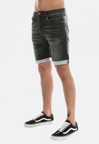 Shorts en denim gris foncé avec une finition délavée, dotés d'un ourlet roulé, de poches avant et d'une fermeture par bouton. Associés à des baskets noires.