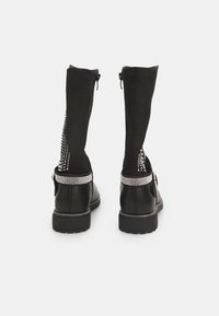 Botas negras de tobillo con caña de ante, embellishments metálicos y un tacón texturizado. Presentan una cremallera lateral para facilitar su uso.