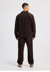 Veste en velours côtelé marron avec pantalon assorti. La veste présente un col et des poignets à boutons, avec des détails de poches à l'avant. Coupe décontractée.