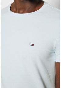 Helles blaues Baumwoll-T-Shirt mit Rundhalsausschnitt und kurzen Ärmeln. Verfügt über ein kleines gesticktes Logo in Rot, Weiß und Marineblau auf der Brust.