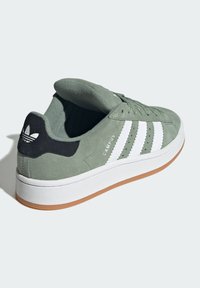 Zelené semišové tenisky s bielymi tromi pruhmi, polstrovaným jazykom, čiernym akcentom na päte, bielou medzipodošvou a hnedou gumovou podrážkou.