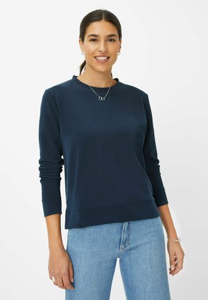 Dunkelblaues Sweatshirt aus weichem Stoff mit langen Ärmeln, Rundhalsausschnitt und geripptem Saum. Kombiniert mit hellblauen Jeans für einen kontrastierenden Look.