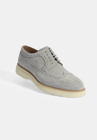 Grijze suède brogue schoen met decoratieve perforaties, vlakke vetersluiting, tan lederen voering en een dikke crèmekleurige rubberen zool.