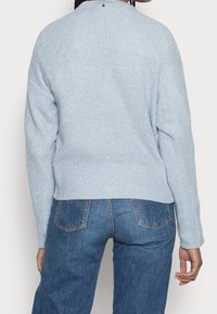 Ljusblå, stickad tröja med ribbad textur, rundad hals och sänkta axlar. Parat med blå denimjeans, med bakfickor.