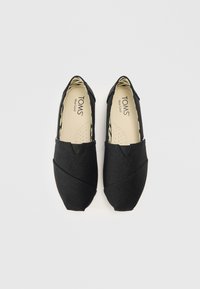 Czarne buty wsuwane TOMS z teksturowanym płóciennym wierzchem, z unikalnym wzorem krzyżującym się i wzorzystą podszewką wewnętrzną.