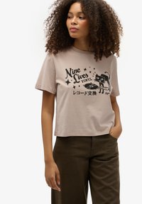 Lyst brun crop-top med grafik af en sort kat og en vinylplade samt tekst på engelsk og japansk. Blødt bomuldsmateriale. Casual pasform.