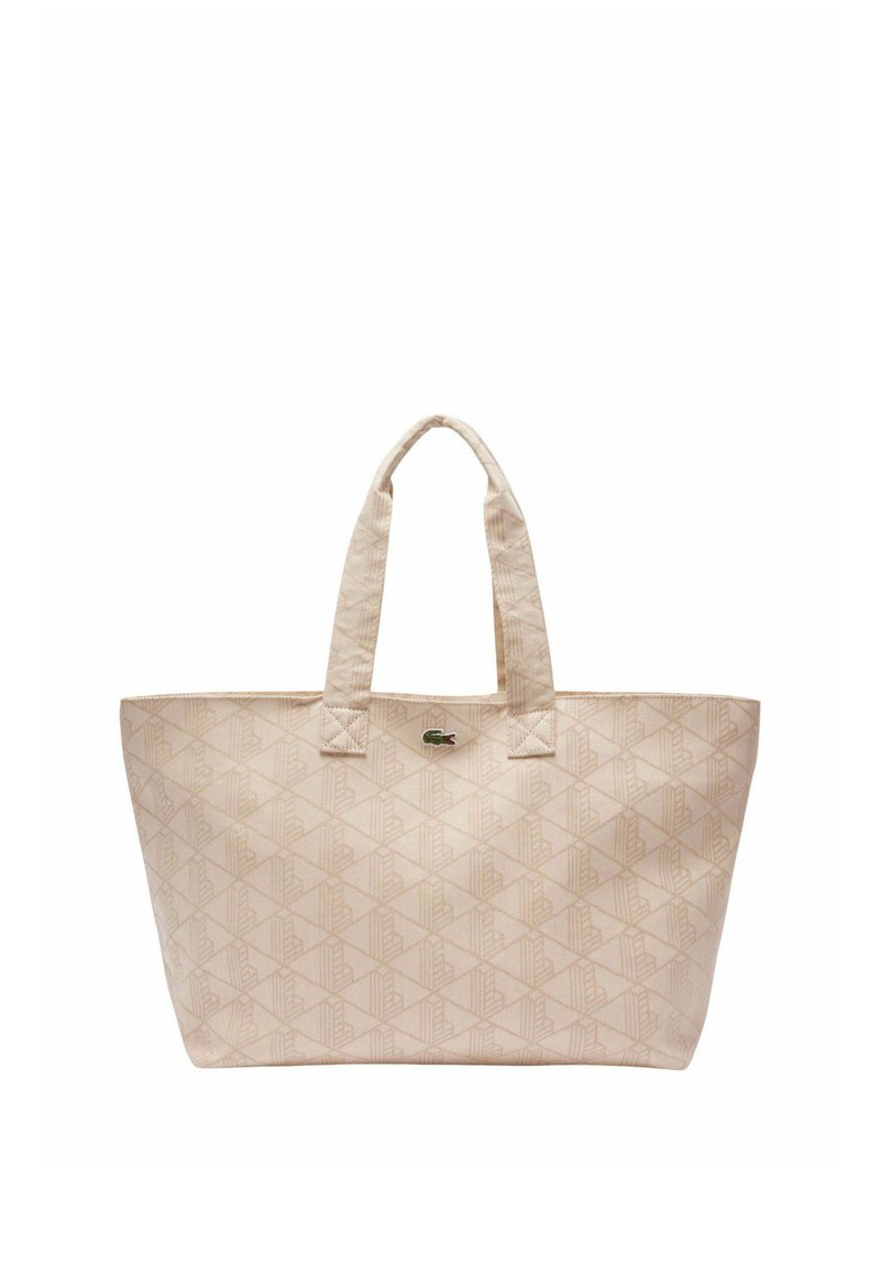 Beige Tragetasche mit geometrischem Muster, zwei Griffen und kleinem grünem Krokodillogo, das nahe der Oberseite zentriert ist.