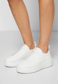 Baskets à plateforme blanches avec lacets portées aux pieds, dotées d'une languette et du logo A|X sur la languette et la semelle.