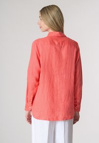 Camicia di lino corallo con colletto a bottoni, maniche lunghe e orlo leggermente curvo. Presenta una vestibilità rilassata e un tessuto strutturato.
