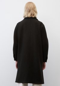 Cappotto di lana nero con un design lungo e dritto, ampio colletto e maniche morbide. Tessuto testurizzato e dettaglio con cucitura centrale sulla schiena.