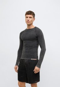 Tričko s dlhým rukávom z tmavého čierneho mäkko pranej tkaniny s hladkou textúrou, s raglánovými švami a dekoratívnou značkovou etiketu na leme.