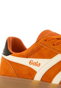 Baskets en suede orange avec des accents en cuir blanc et un empiècement de talon noir. Présente une surface texturée et un logo Gola sur la languette.