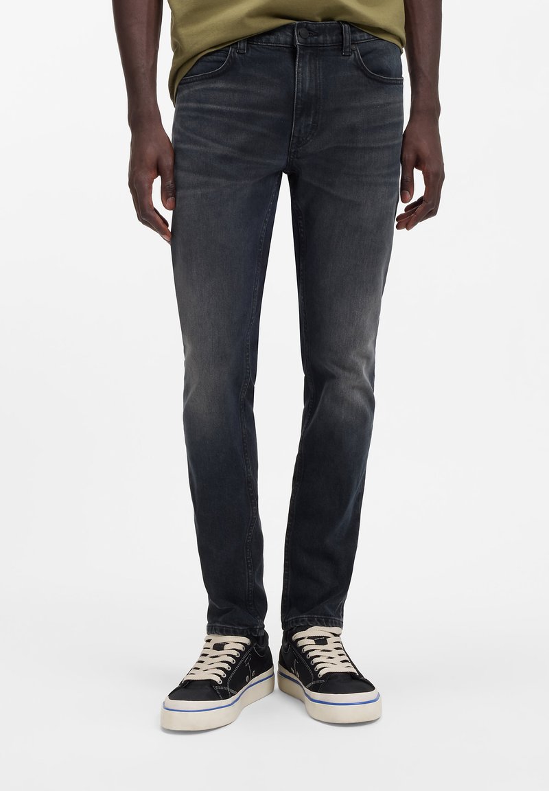 Tummanharmaat, kapealahkeiset farkut, joissa on viisi taskua, haalistunut pinta ja klassinen ompelu. Yhdistetty mustiin tennareihin, joissa on kermaiset nauhat.