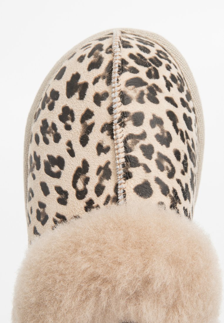 Hausschuh mit Leopardenmuster und beige Wildleder-Obermaterial, weicher beiger Fellfutter und dekorativer Naht entlang der Naht. Rundliche Form, gemütliche Textur.
